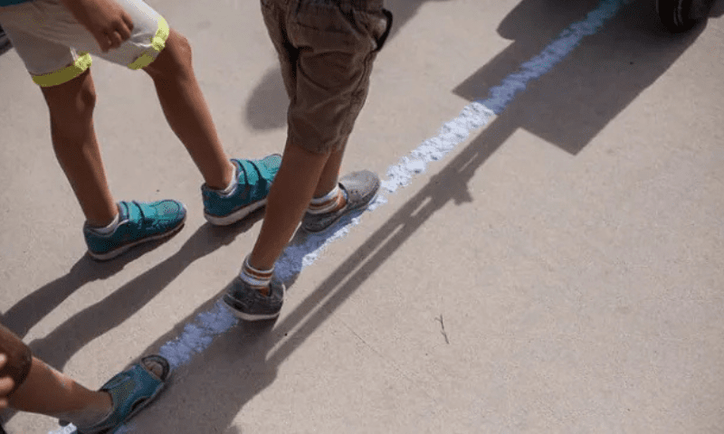 Close-up image of three people walking on a white line, painted on a concrete floor.