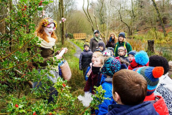 Performer in costume with a group of children. Three adults observing. Forest setting.