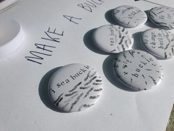 Photo of a set of badges in black and white saying 'I sea Buckie' and 'Sea Change Buckie'.