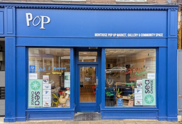 Photo of the PoP Shop shopfront with posters for the Sea Change project in the window and words saying 'What if Montrose was thriving?'