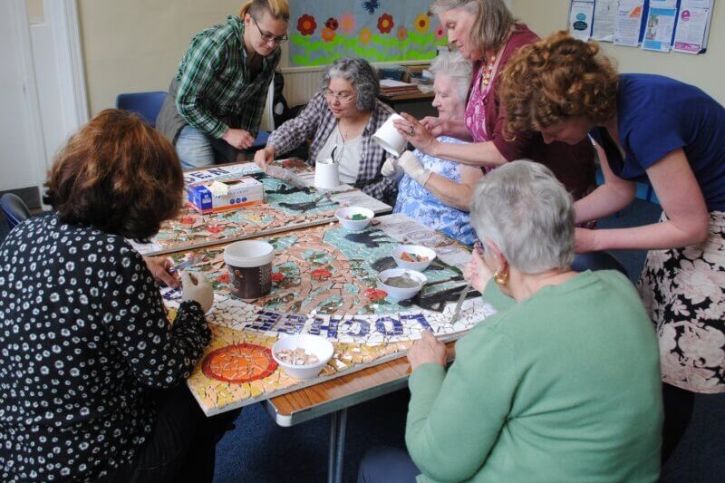 A group of people sitting at a table working on a mosaic.