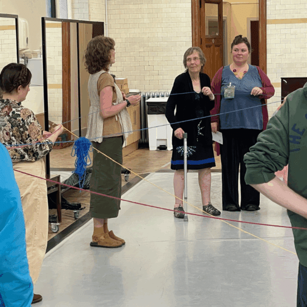 Six people creating a web with red, yellow and blue yarn.