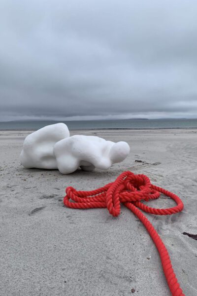 Red rope and a white form on a beach.