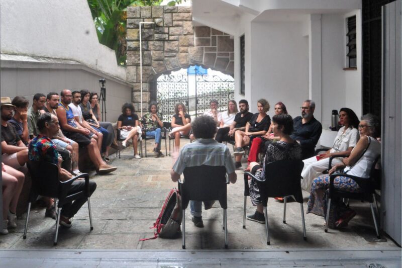 A medium group of people sit in a circle in a courtyard.