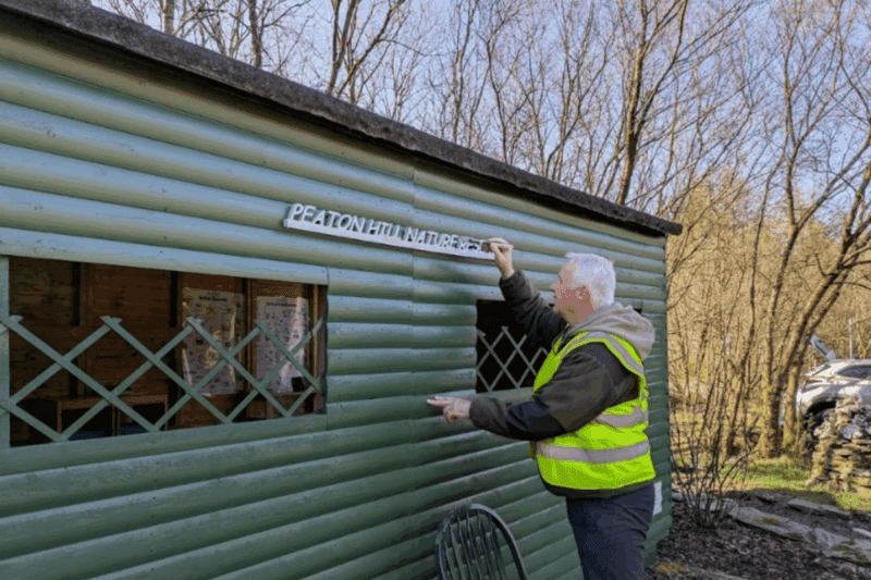 Man painting 'Peaton Hill Nature Reserve' on a shed