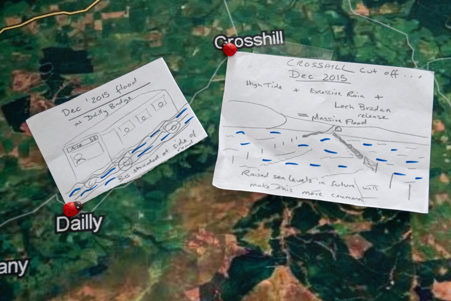 Two drawings stuck to a map. One drawing shows a bus stranded on the side of the road due to flooding. The other drawing shows flooded roads and fields.