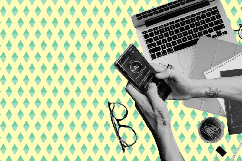 A cut out photo of a pair of hands using an AI app on a phone with laptop and notebooks.